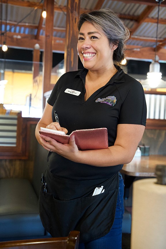 A smiling woman taking an order.