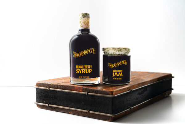 A bottle of huckleberry syrup next to a jar of huckleberry jam.